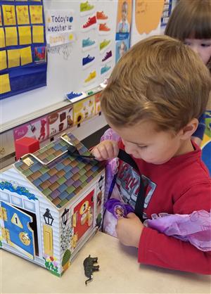 Student using fine motor skills while using a key to open a toy house. 